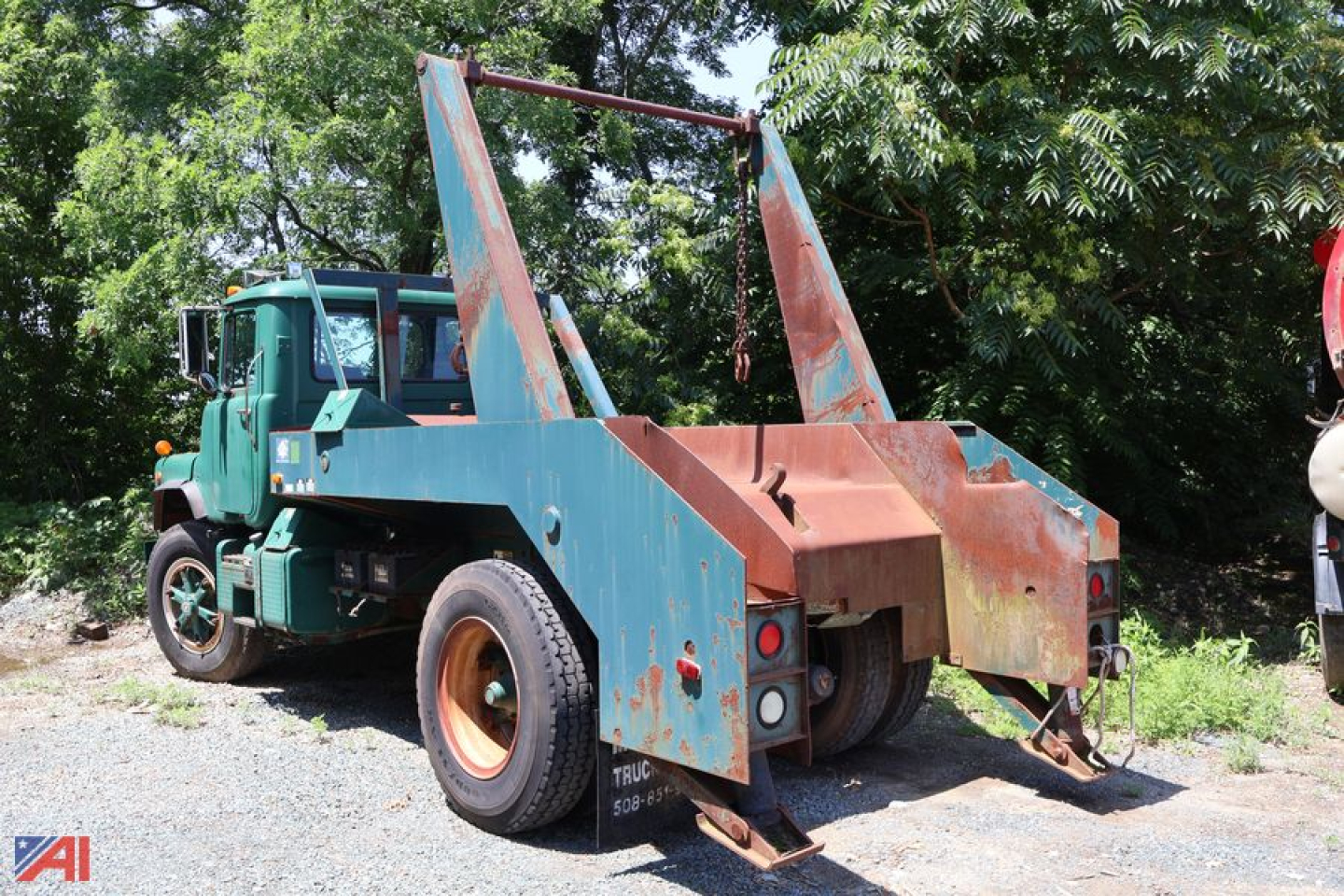 Truck with a hydraulic winch and hook arms on a blue bed; green Mack DM688X truck cab; rear view shows lift arms and towing/winch setup.