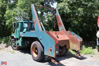 Truck with a hydraulic winch and hook arms on a blue bed; green Mack DM688X truck cab; rear view shows lift arms and towing/winch setup.