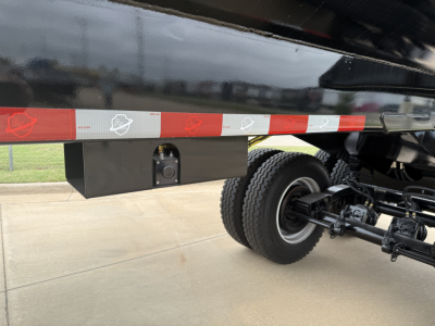 Truck trailer undercarriage showing black toolbox and dual rear wheels with suspension, side rail with reflective tape.