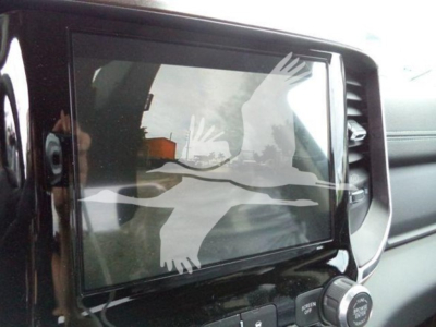 Truck interior dashboard with a large touchscreen display showing a watermark of overlapping white birds in flight; reflection in screen.