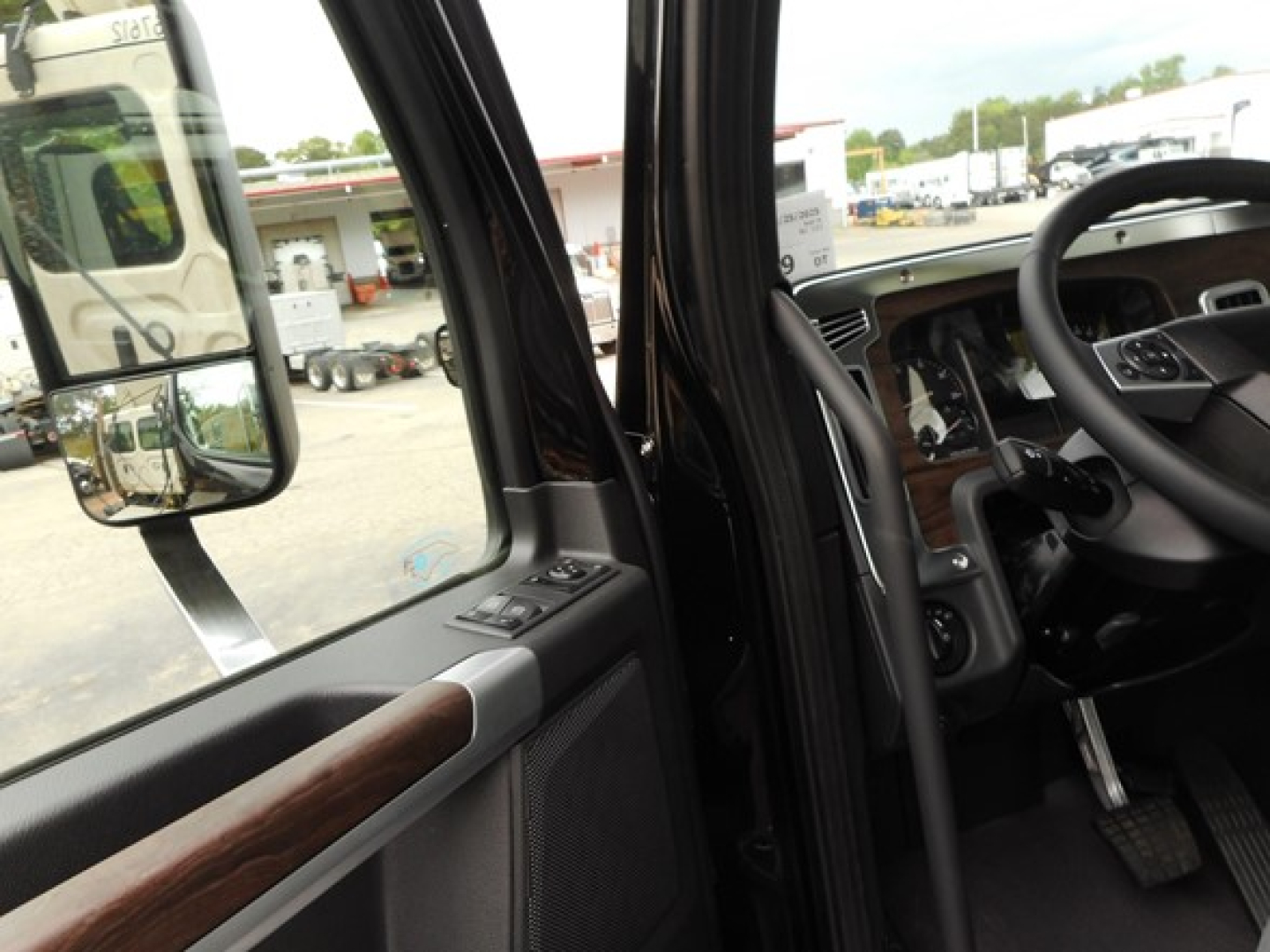 Interior cab view of a 2026 Western Star 49X showing steering wheel, dashboard, and door panel with wood trim and window controls.