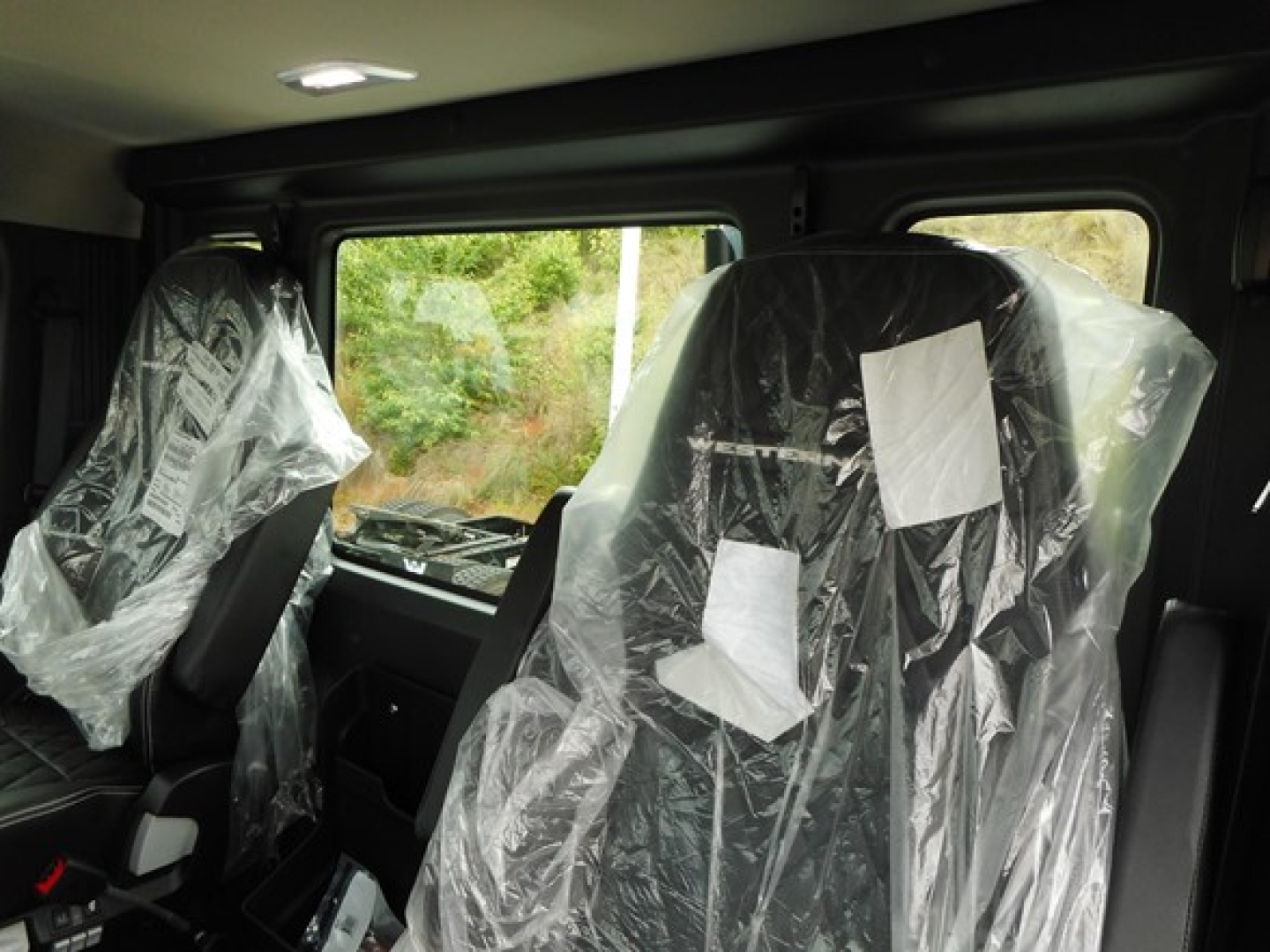 Interior of a new Western Star 49X day cab showing driver and passenger seats wrapped in protective plastic and a large side window.