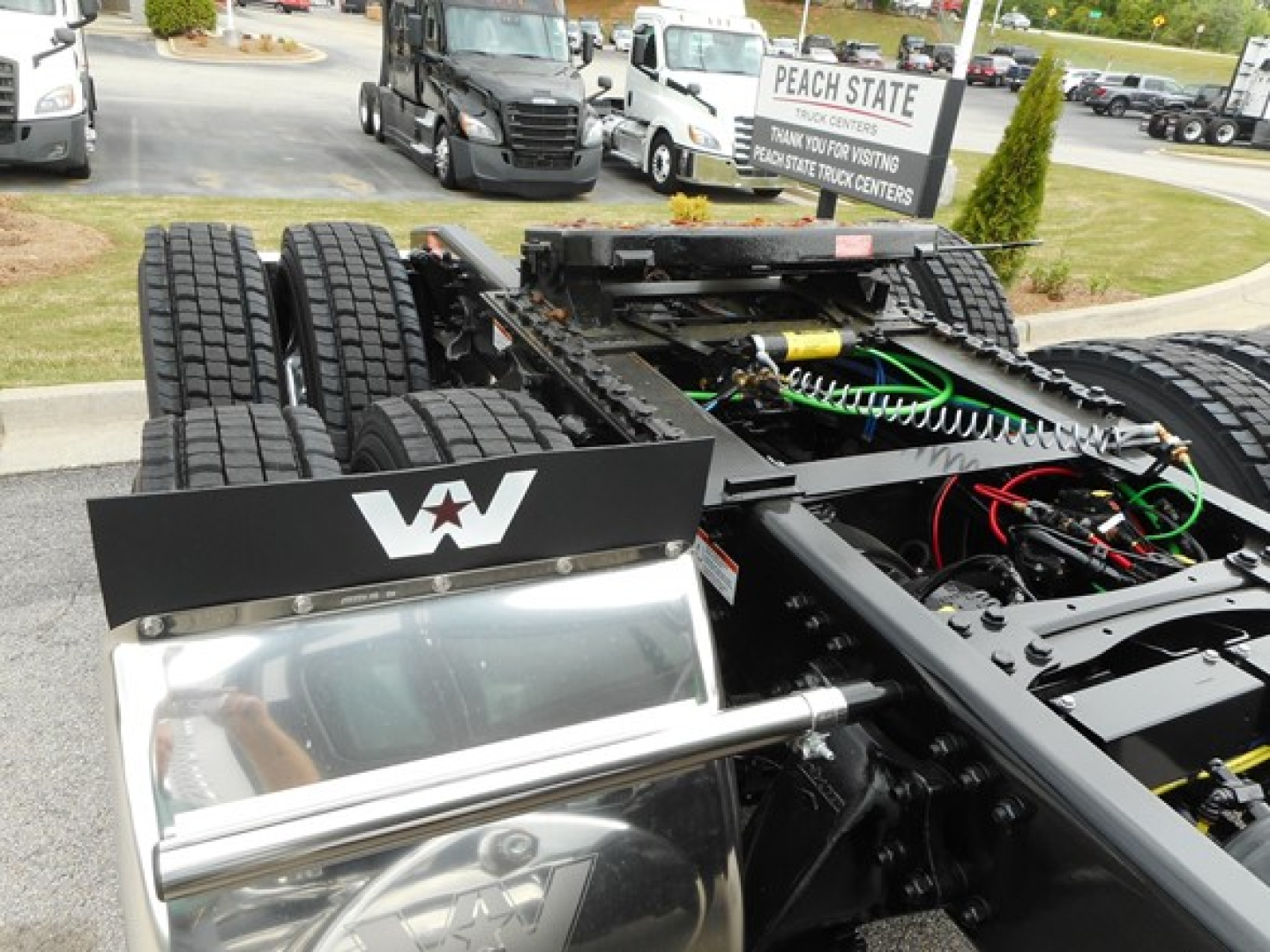 Semi truck chassis showing dual rear axles, Fifth wheel, and exposed hydraulic lines in the engine bay area of a 2026 Western Star 49X cab chassis.