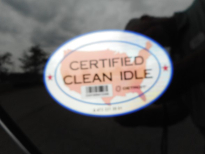 Certified Clean Idle sticker on vehicle window with barcode and map outline.