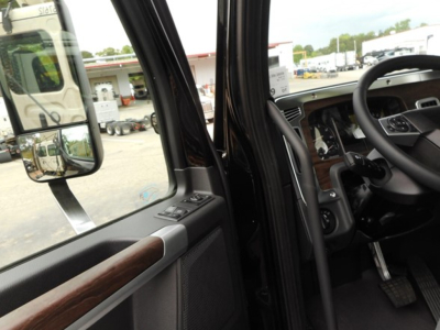 Interior cab view of a 2026 Western Star 49X showing steering wheel, dashboard, and door panel with wood trim and window controls.