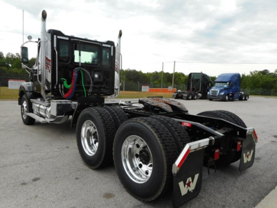 Semi truck chassis in daylight with dual rear axles and chrome exhaust stacks, cab with green hoses, and a blue truck in distance.