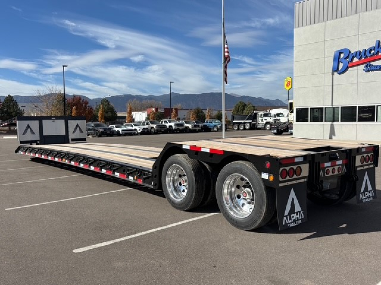 Alpha trailer lowboy with detachable double drop and swingouts, dual rear axles, flat deck, rear lights, and mud flaps showing Alpha branding in a dealership lot.