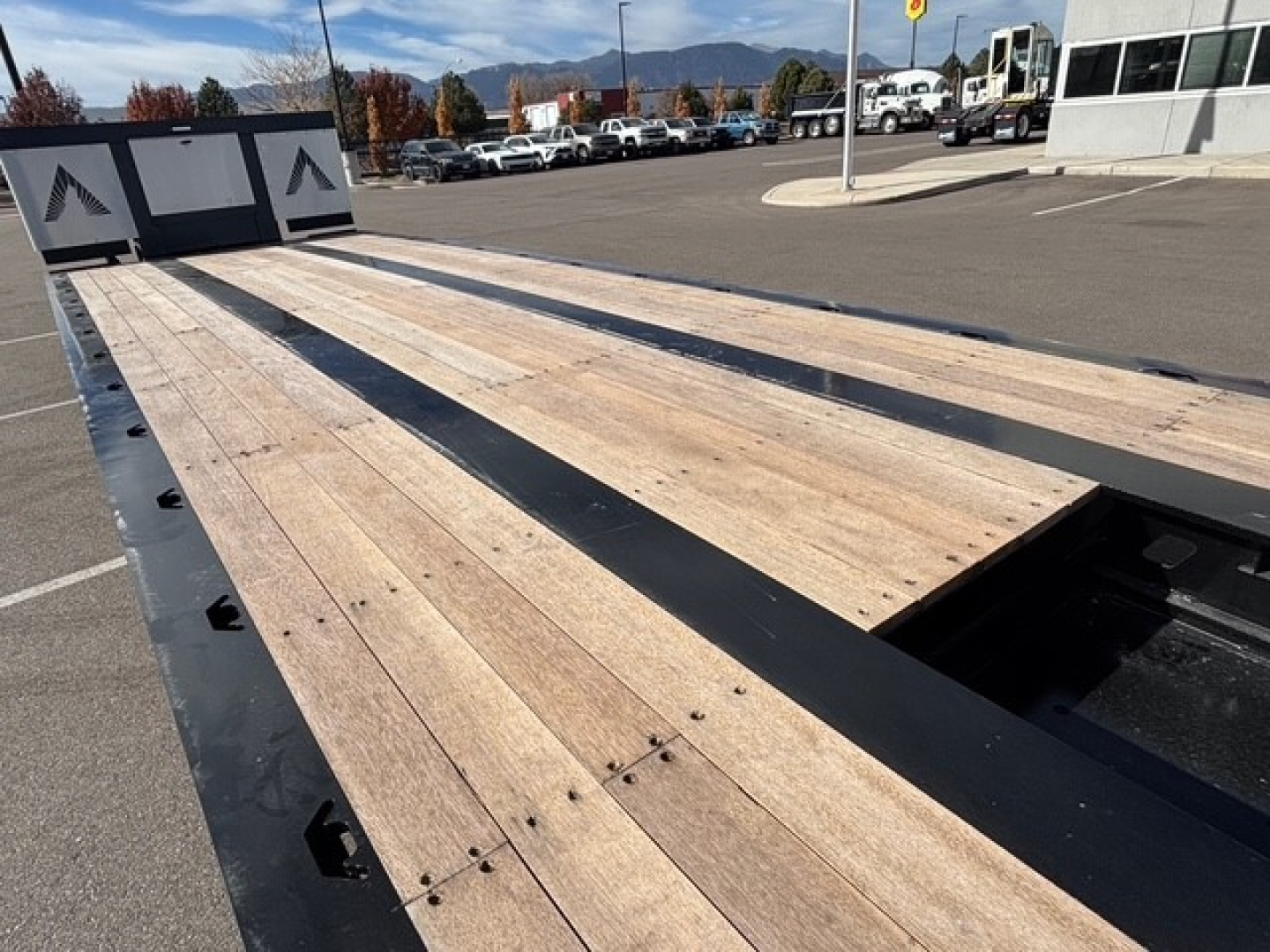 Lowboy trailer bed with wooden planks and steel supports, open areas showing swingout and drop mechanism, long flat deck in an outdoor lot.