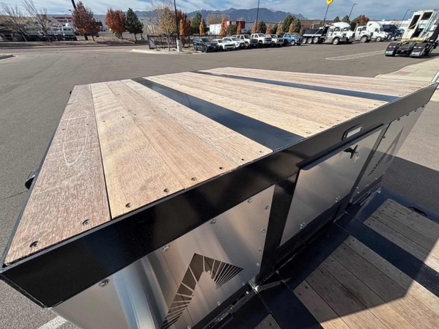 Trailer deck of 2027 Alpha A80MG Mech Detach Double Drop with Swingouts showing wooden planks on top and metal side panels.