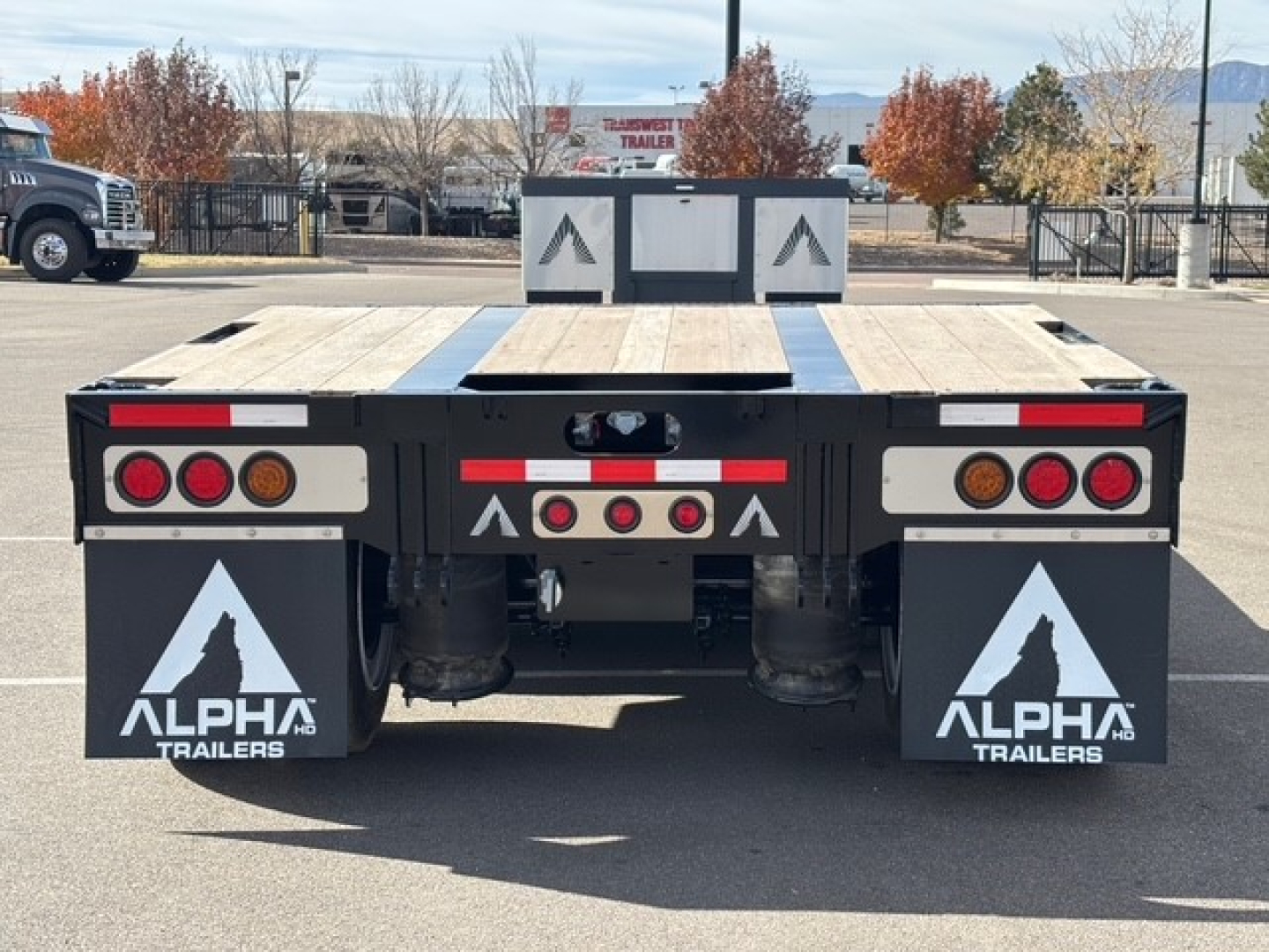 Trailer rear view of a 2027 Alpha A80MG lowboy with swingouts, dual axles, and mudflaps reading ALPHA TRAILERS; reflective markings and taillights visible.