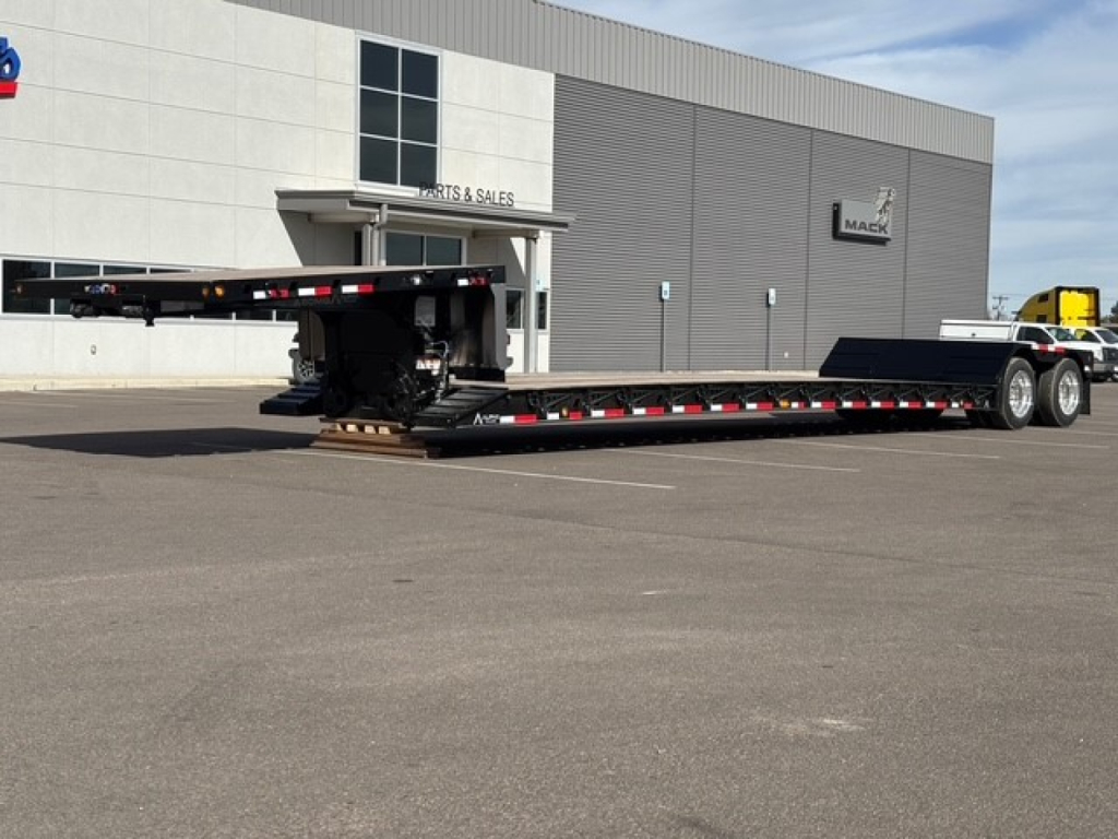 Lowboy trailer with swing-out, double-drop deck in front of a dealership building.