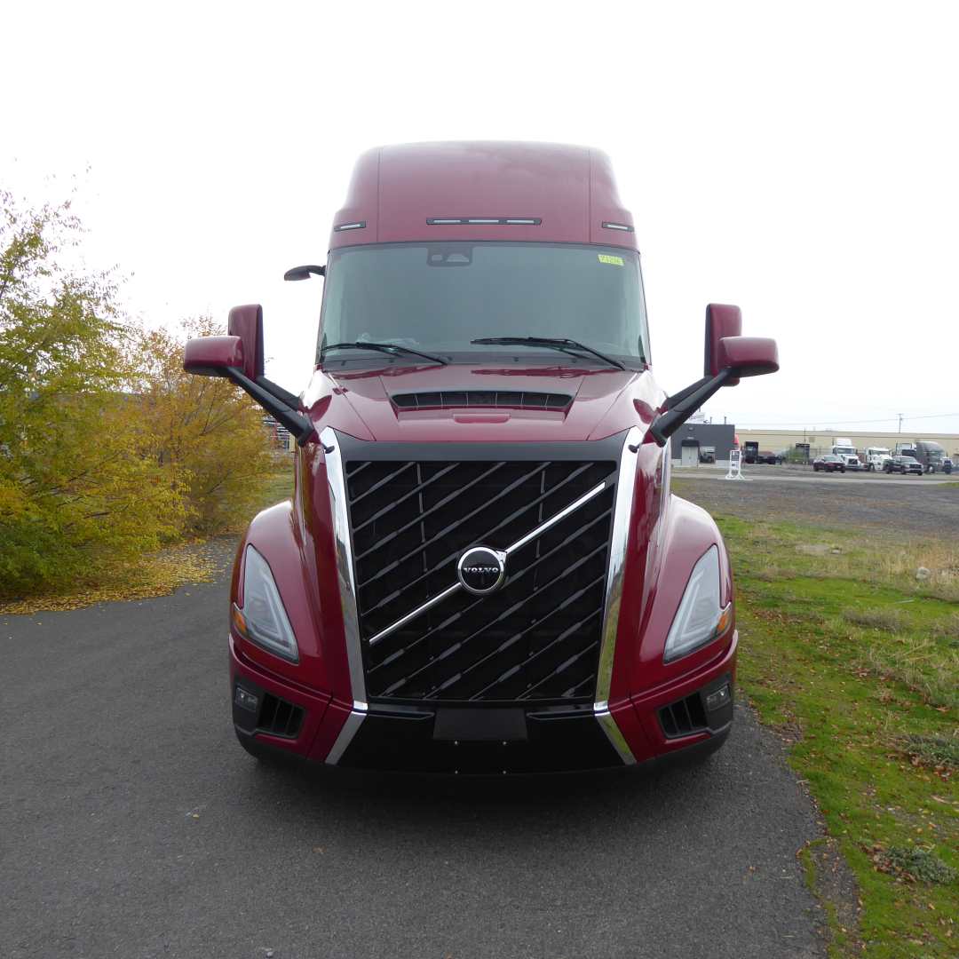 Front view of a maroon Volvo VNL64T860 sleeper cab truck with large black chrome grille and Volvo emblem, daytime outdoor lot.