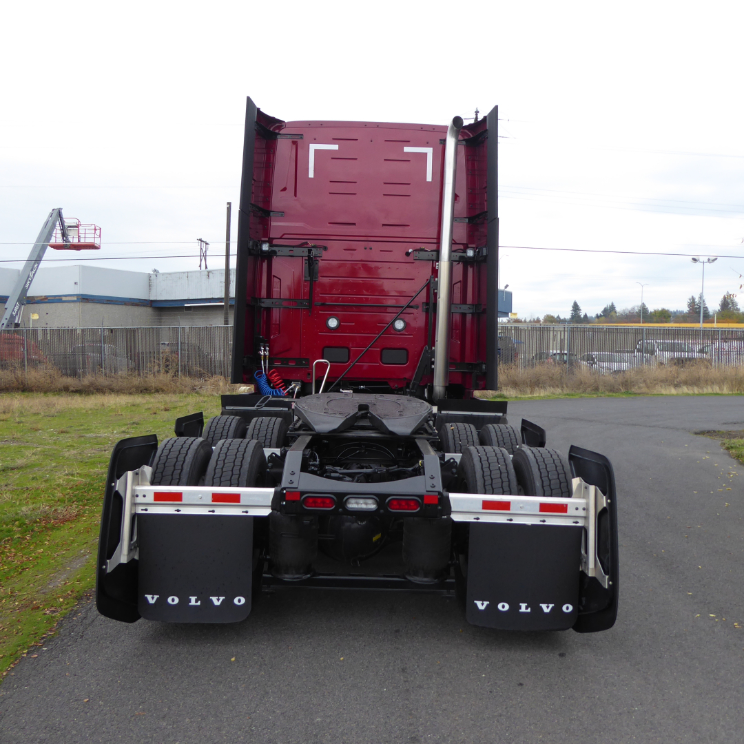 Rear view of a red Volvo VNL64T860 truck tractor showing fifth wheel, dual rear axles, and black mud flaps with VOLVO text.