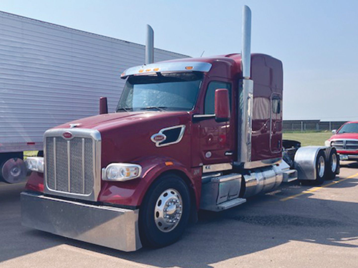 Peterbilt 567 UltraCab truck in maroon with high-roof sleeper, chrome grille, dual tall air cleaners, chrome bumper, and side fairings parked in lot.