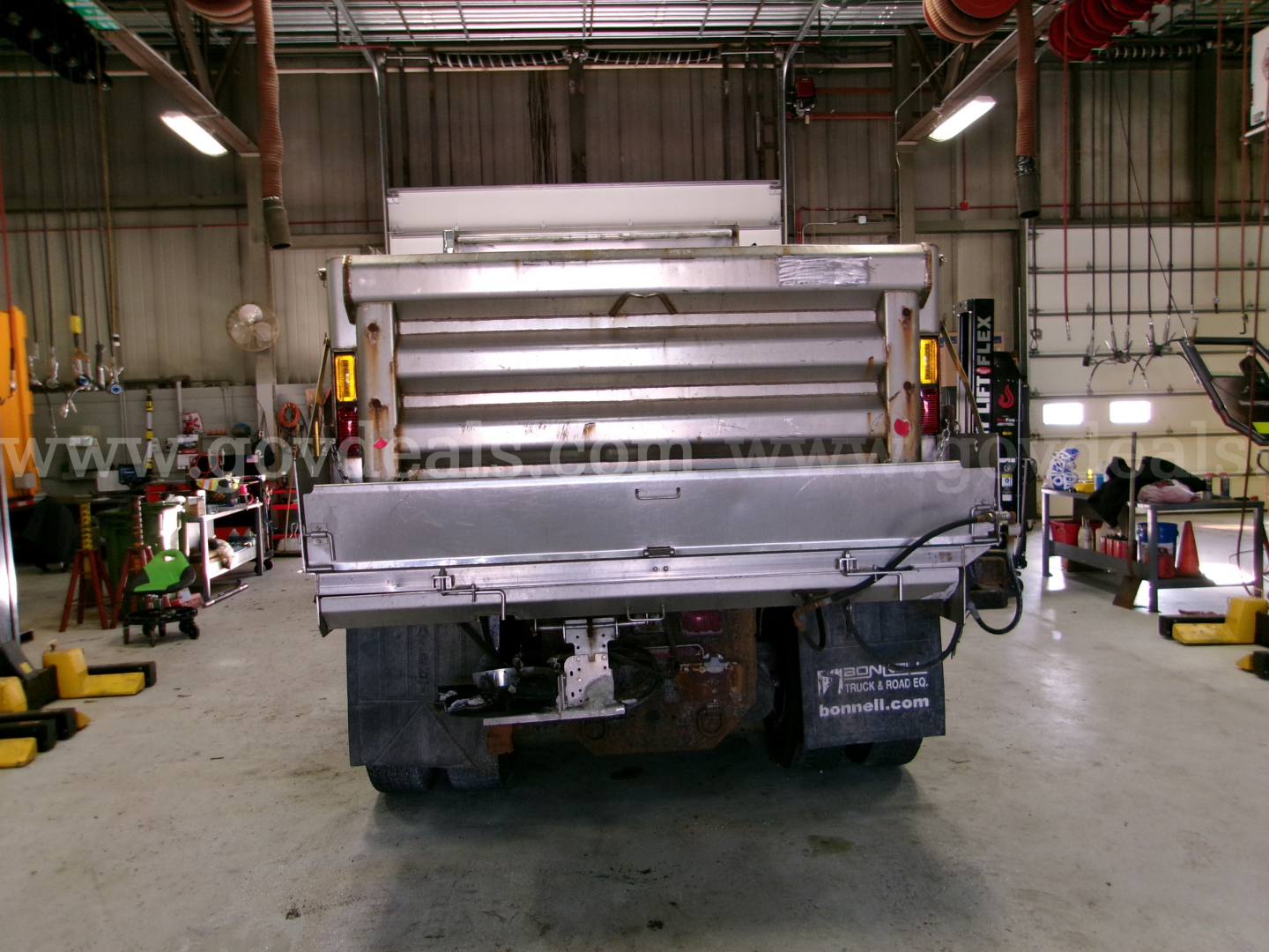 Dump truck rear showing cargo bed and bumper with lights in a workshop.
