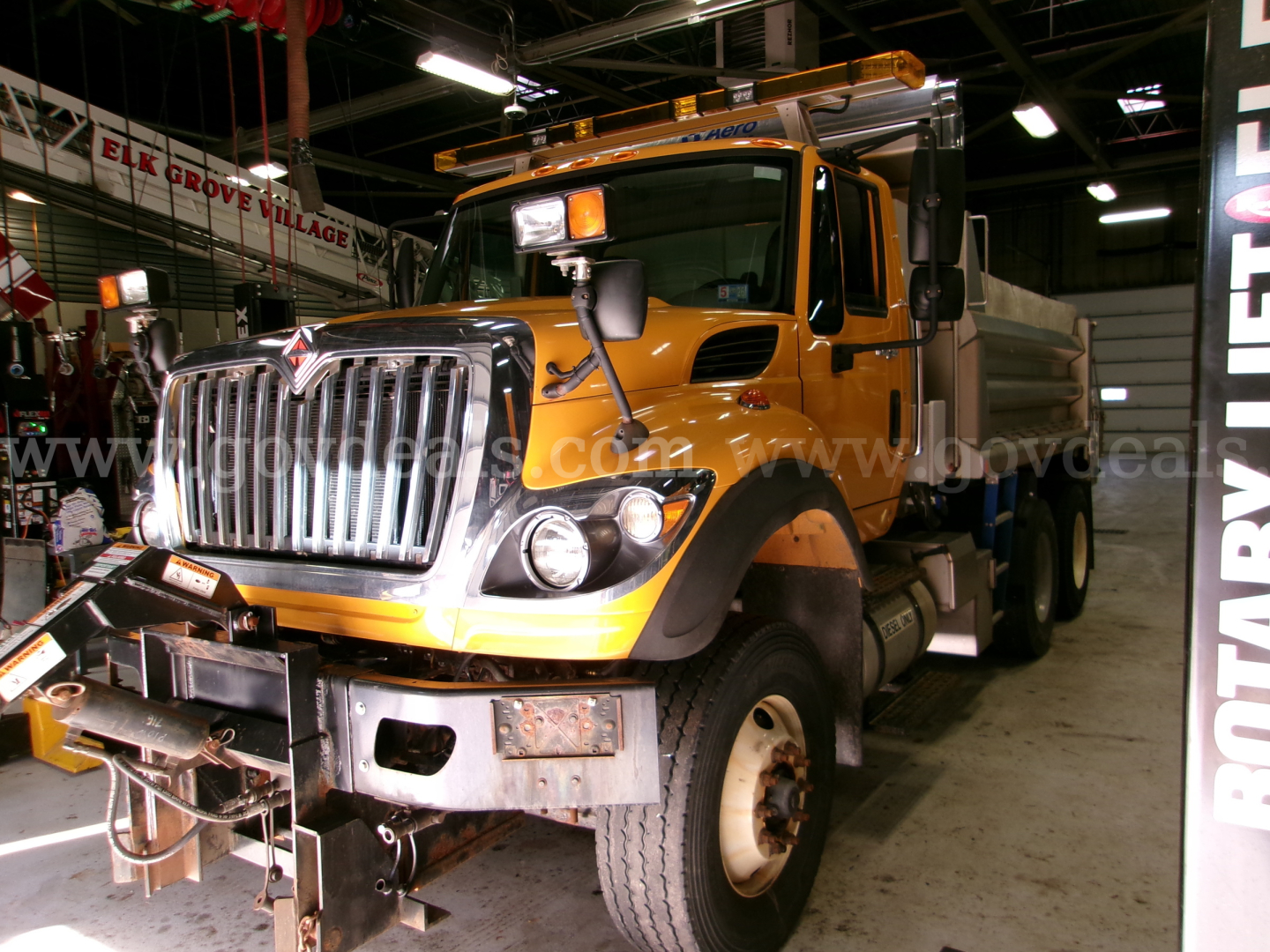 International dump truck with orange cab and chrome grille in a showroom showing front bumper and cargo bed.
