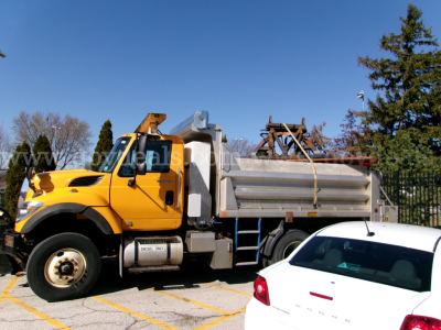 Dump truck with yellow cab and silver dumping bed in a parking lot, side view.