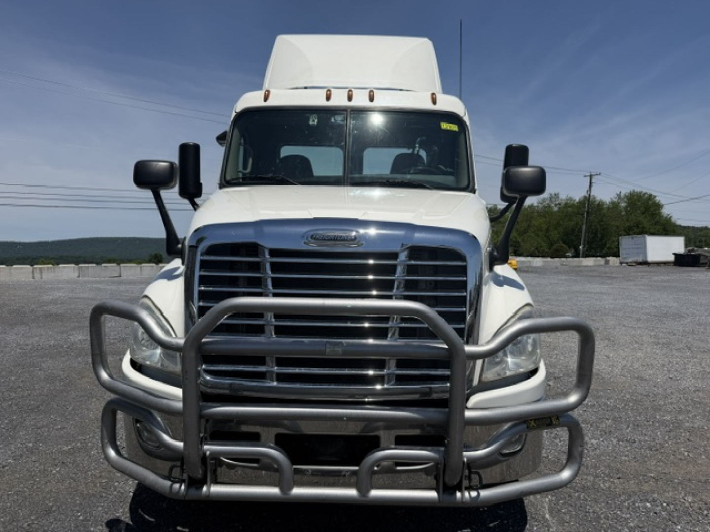 Front view of a Freightliner Cascadia CA125DC tractor with a heavy-duty grille guard and bumper in a gravel lot.