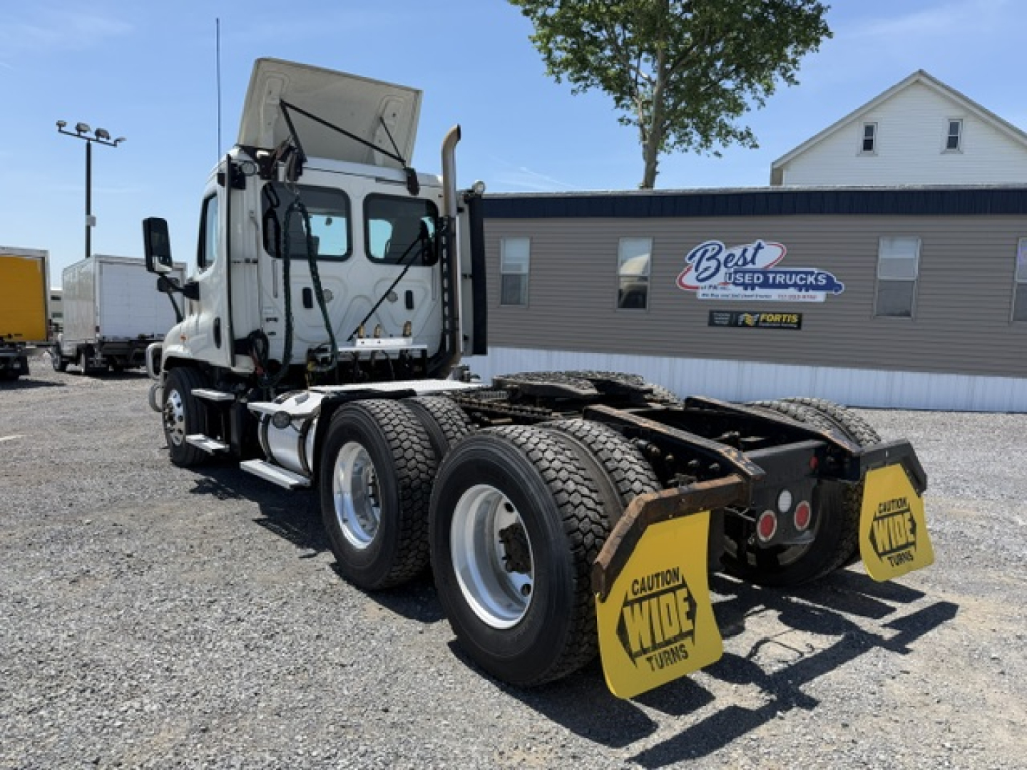 Freightliner Cascadia CA125DC tractor rear view showing dual rear axles and wheel chocks with 'Wide Turns' caution on yellow plates.