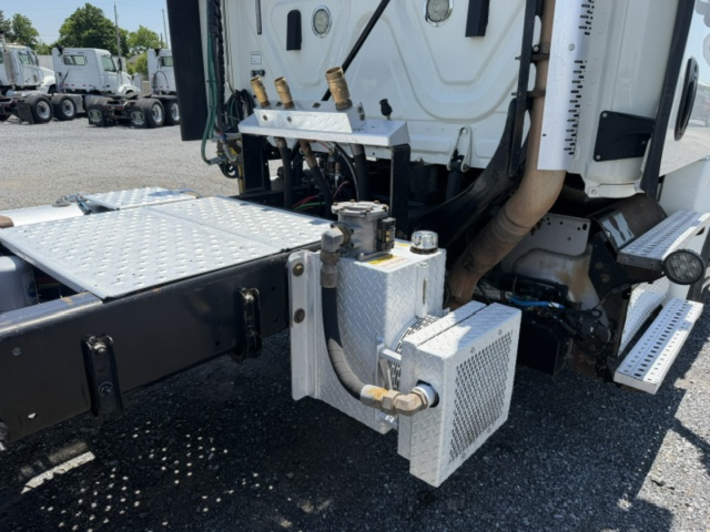 Freightliner Cascadia CA125DC engine bay area with aluminum toolbox and hydraulic components, showing a metal rectangular reservoir and piping.
