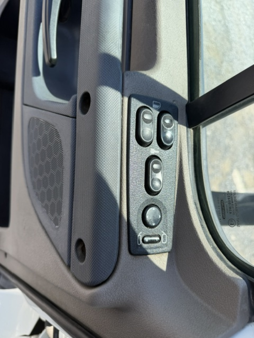 Truck cab interior controls on door panel including window switch buttons and mirror adjustment, with speaker grill in view.