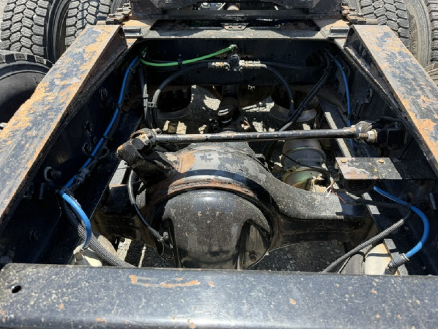 Freightliner Cascadia chassis view showing drivetrain components and suspension in the engine bay area; visible hoses, cables, and frame rails.