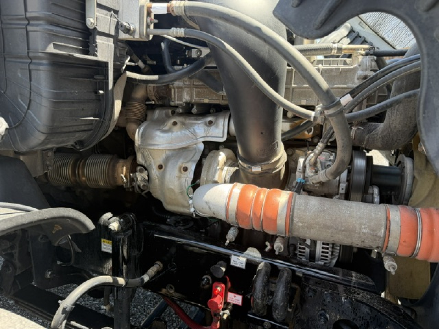 Engine bay interior of a Freightliner Cascadia shows intake hoses, turbocharger, belts, and routing hoses in view with orange insulated hose nearby.