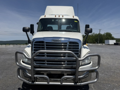 Front view of a Freightliner Cascadia CA125DC tractor with a heavy-duty grille guard and bumper in a gravel lot.