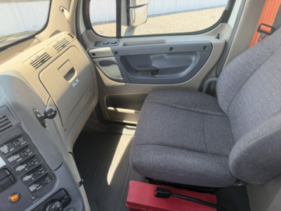 Cab interior of a Freightliner Cascadia CA125DC showing steering area and passenger seat with grey fabric and door panel