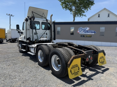 Freightliner Cascadia CA125DC tractor rear view showing dual rear axles and wheel chocks with 'Wide Turns' caution on yellow plates.