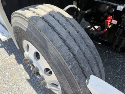 Truck front tire close-up view on Freightliner Cascadia CA125DC showing dual rear tires and wheel hub. 
