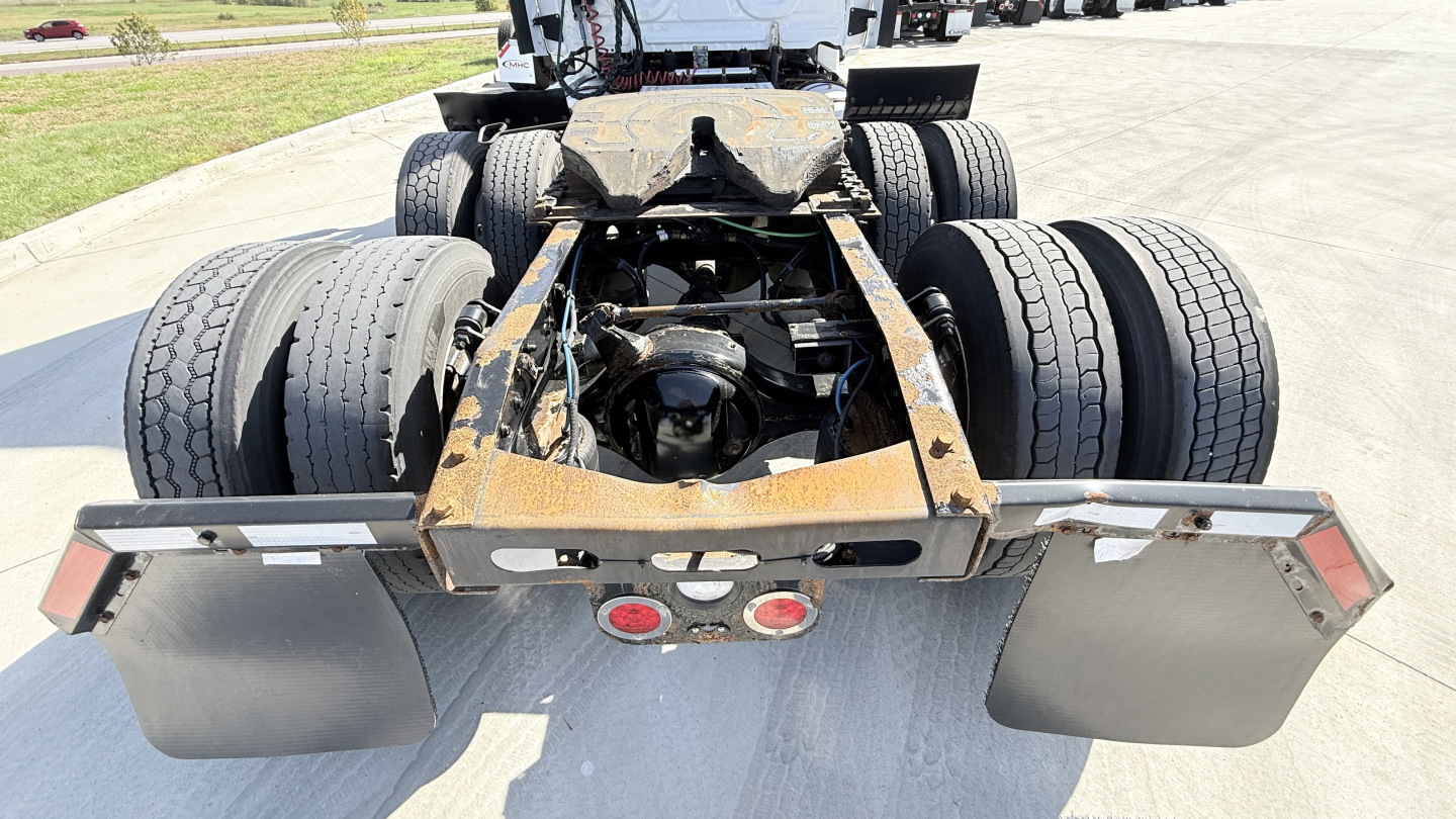 Rear view of a Freightliner cab and chassis showing dual rear axles with large tires, rusty frame, and mudflaps.