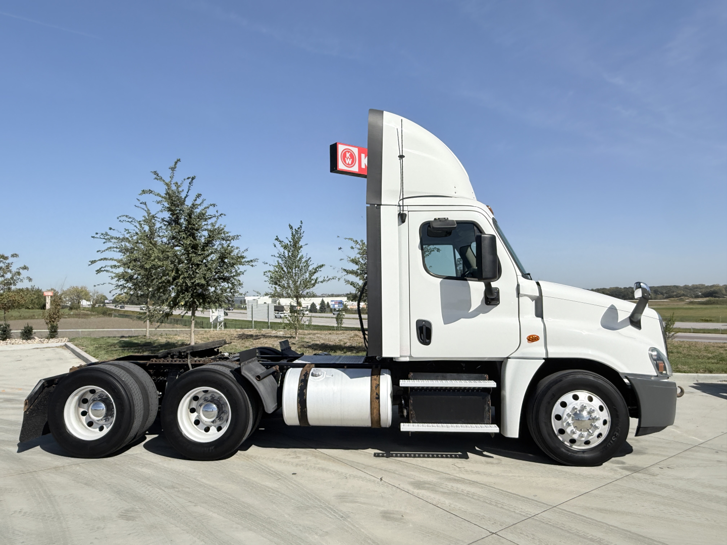 Truck side view showing a white Freightliner CA12564DC tractor with sleeper cab, dual rear axles, fuel tanks, and exhaust, exterior text not legible.