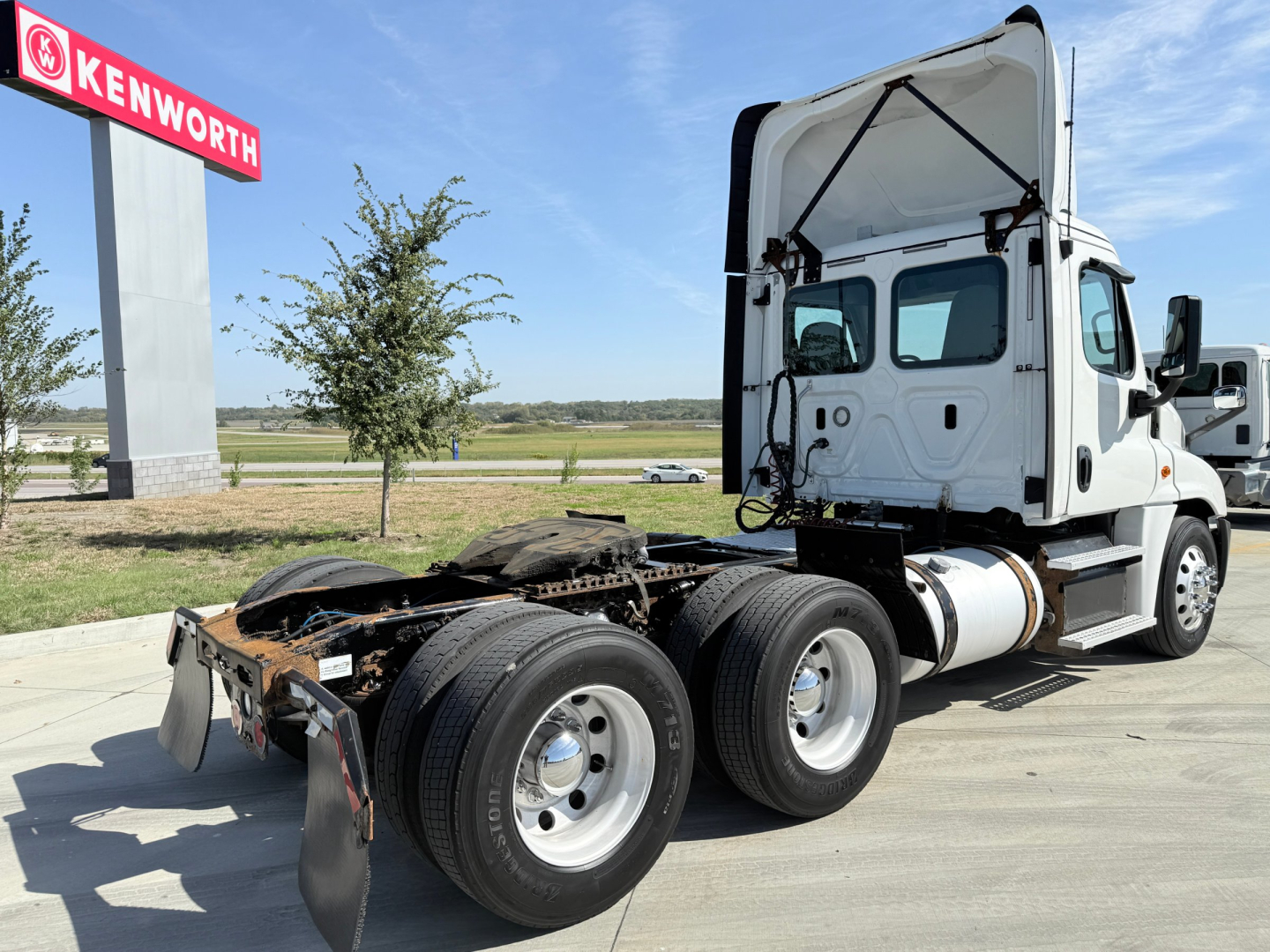 Freightliner CA12564DC tractor unit side view showing rear suspension and cab, white truck with open sleeper area, fuel tanks, and dual rear axles.