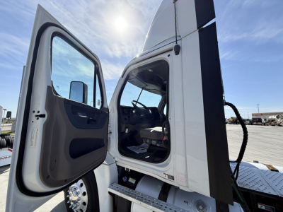 Truck cab interior with open door showing Freightliner CA12564DC style cab access, dashboard and steering wheel visible.