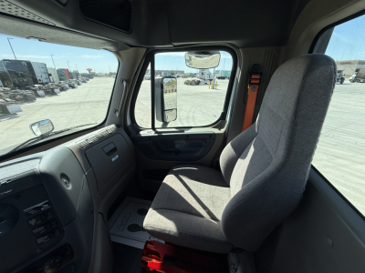 Truck cab interior showing driver's seat and dashboard of a Freightliner CA12564DC with steering wheel and window view.