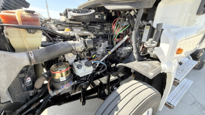 Freightliner CA12564DC engine bay showing hydraulic reservoir, hoses, and wiring harness between cab and engine compartment.