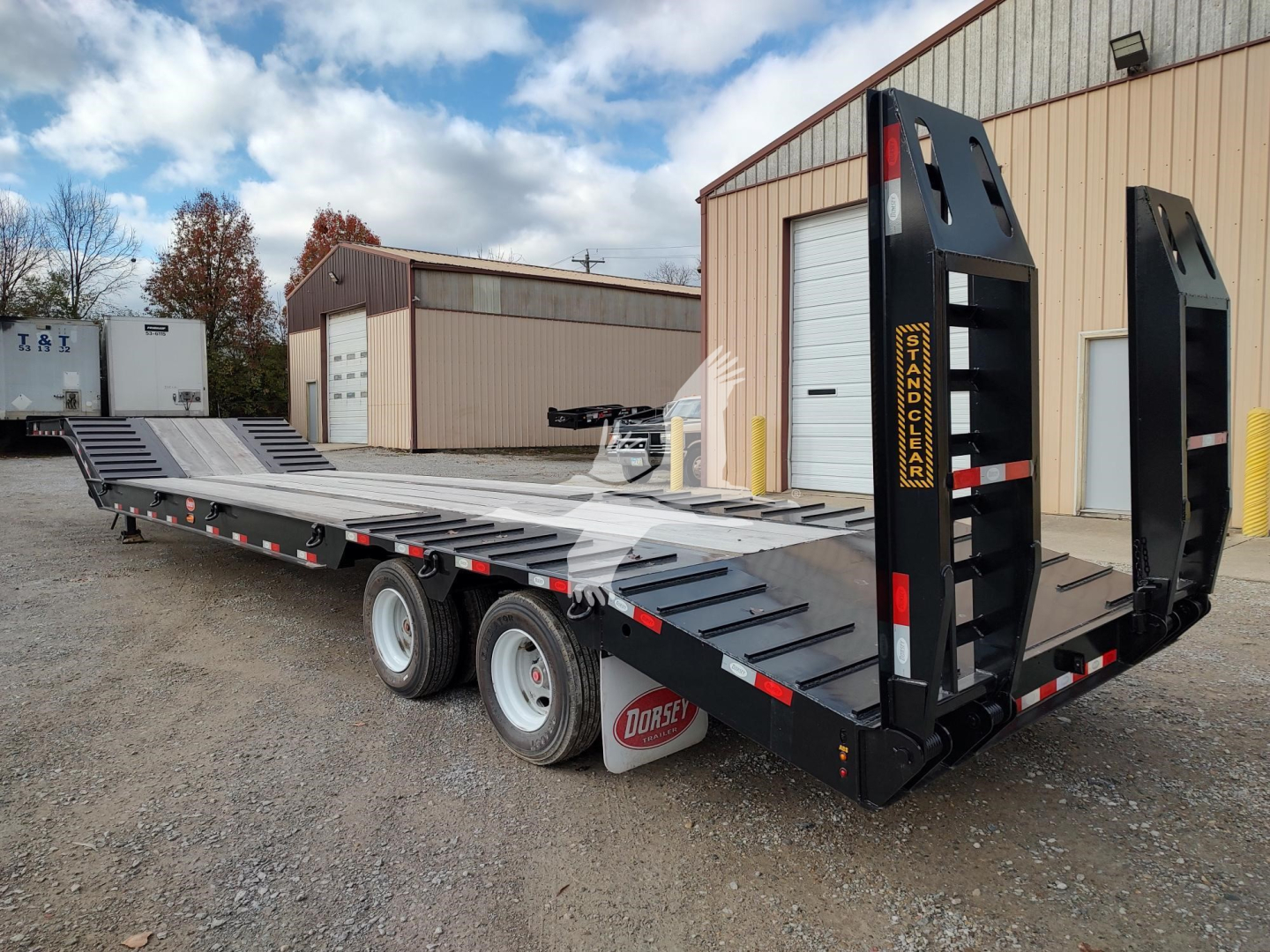 Trailer in a lot showing a low-boy drop deck with tandem axles and ramp legs, black with yellow accents and Dorsey branding on the ramps.