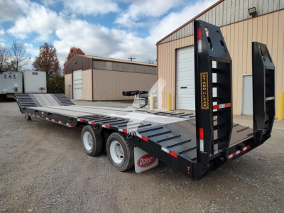 Trailer in a lot showing a low-boy drop deck with tandem axles and ramp legs, black with yellow accents and Dorsey branding on the ramps.
