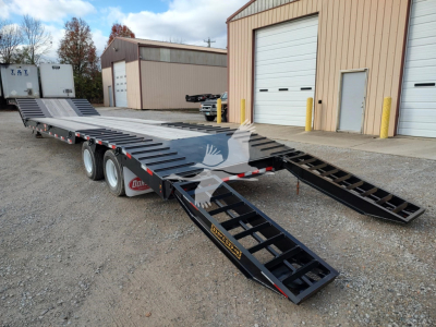 Low-angle view of a black Dorsey LB35-33CS drop deck trailer with folding ramps extended in a yard.