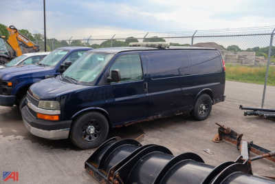 Chevrolet Express full-size cargo van in a used condition with dark blue paint, parked on lot among other vehicles and equipment.