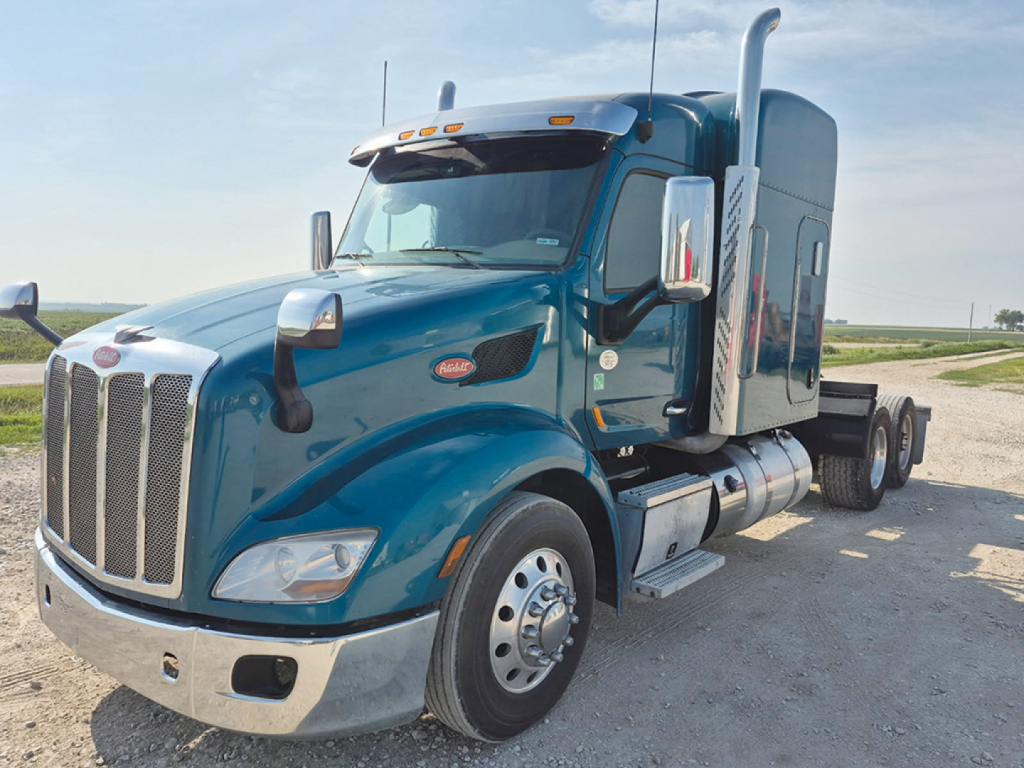 Peterbilt 579 UltraCab tractor in teal blue, front left view, showing large grille, side mirrors, fuel tanks, and sleeper cab exhaust stacks.