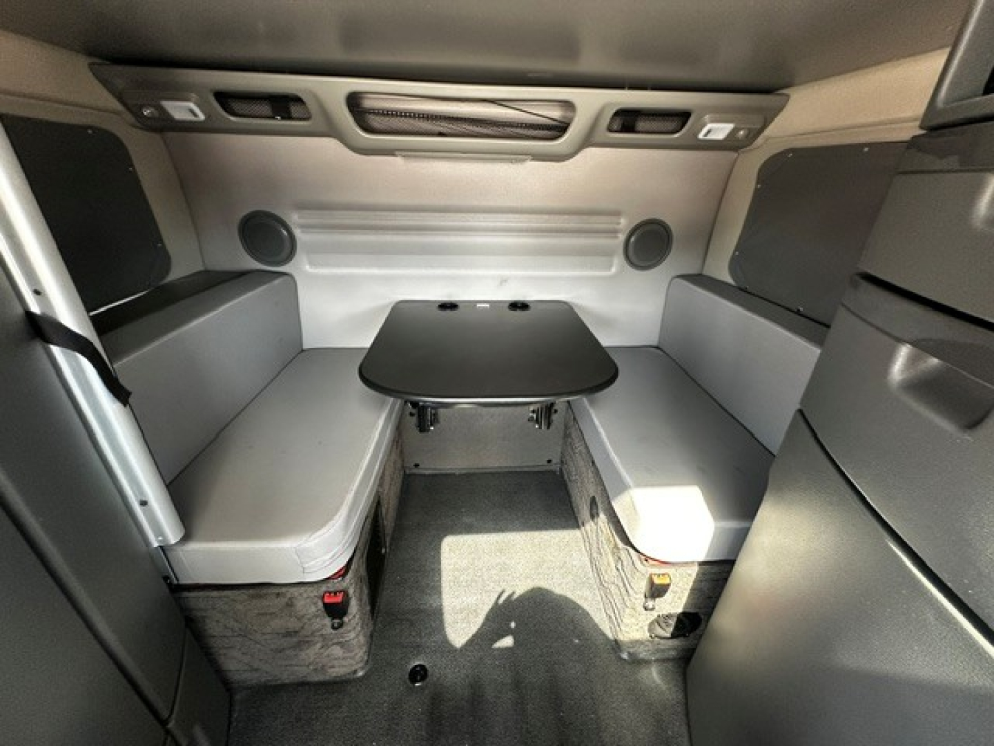 Volvo VNL interior showing sleeper cab with U-shaped benches, center table, overhead storage, and windowed panels.