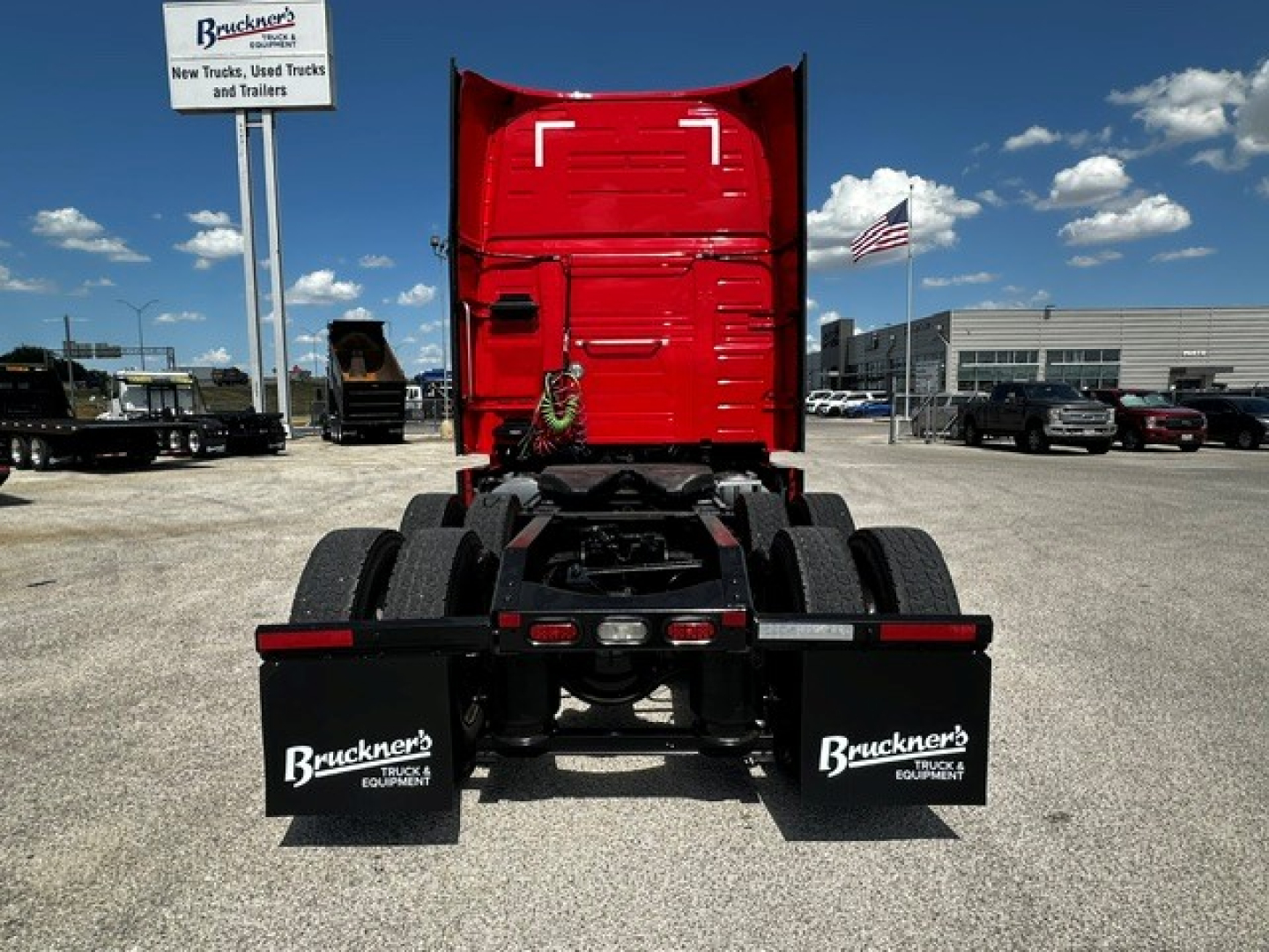 Truck rear view showing Volvo VNL64T860 sleeper cab with fifth wheel and dual rear axles, mud flaps labeled Bruckner's Equipment, dealership lot in background.