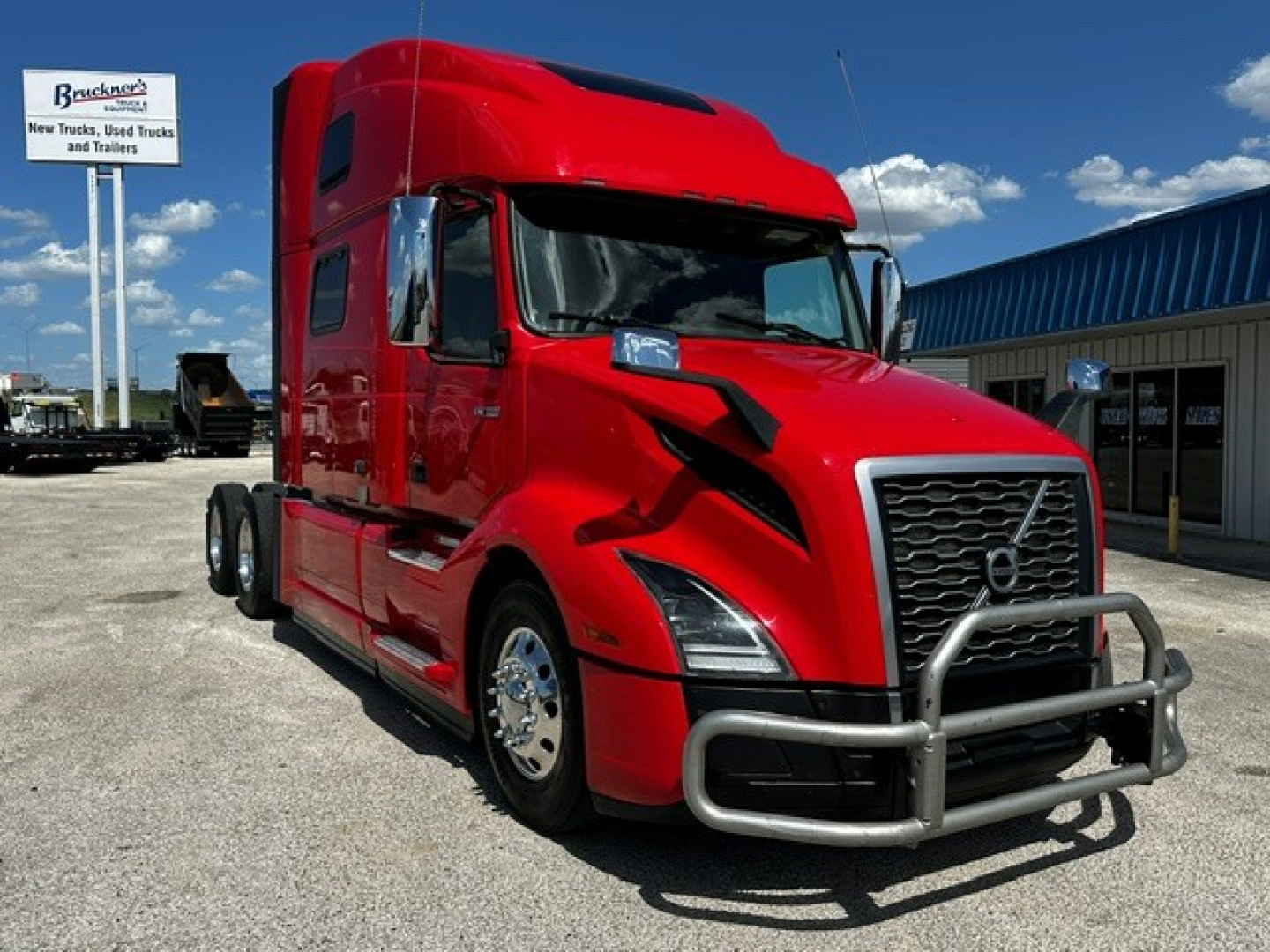 Red Volvo VNL64T860 semi truck with front bull bar and aerodynamic cab in a dealership lot.