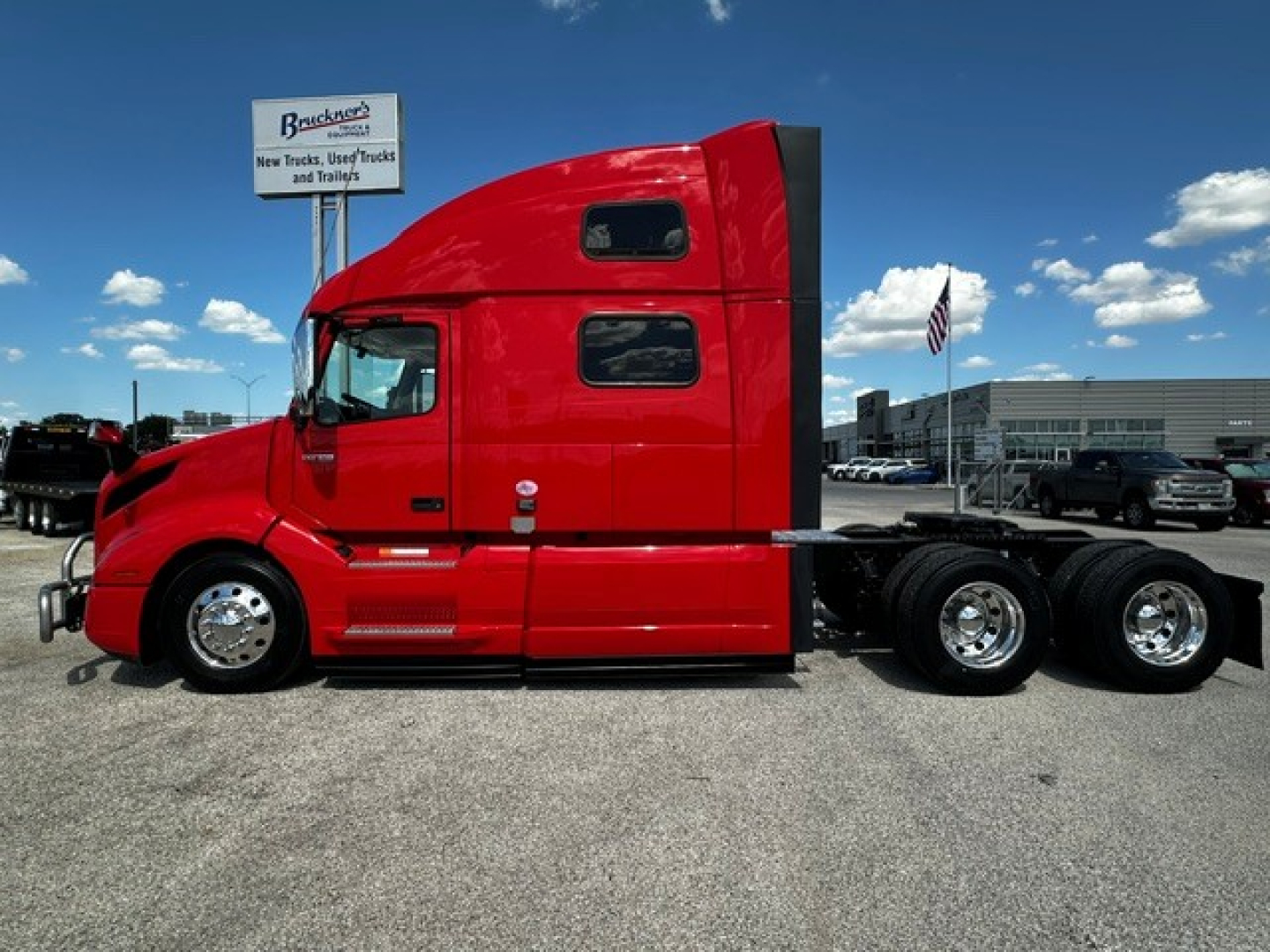 Side view of a red Volvo VNL64T860 truck tractor in a dealership lot showing cab with sleeper window and dual rear axles.