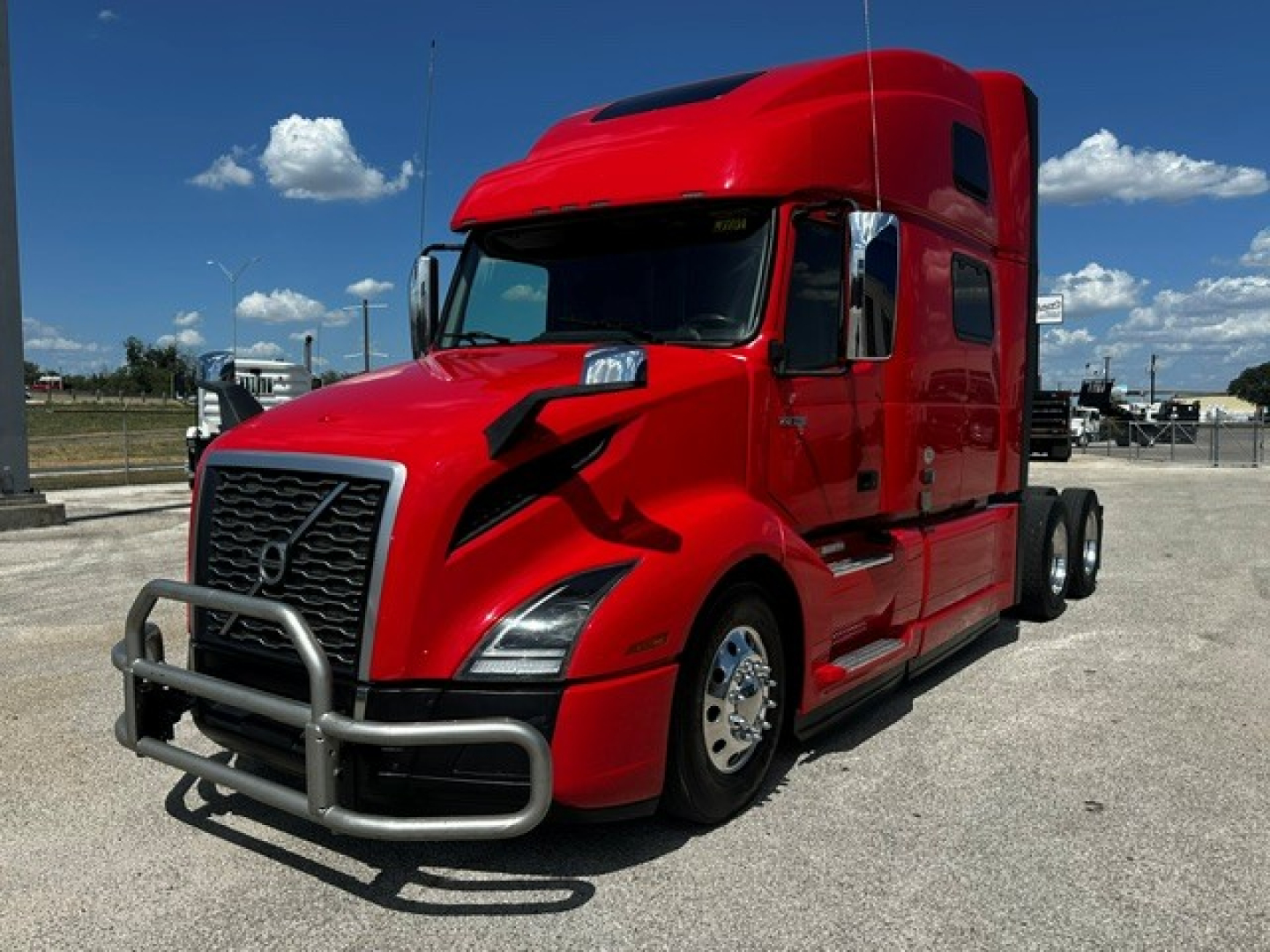 Volvo VNL64T860 sleeper cab truck in red, front grille guard, side steps, chrome wheels, long hood, daytime setting.