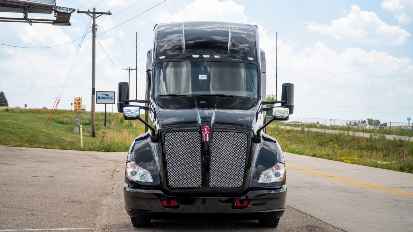Kenworth T680 sleeper cab front view with dual chrome grille and large windshield, black paint, daytime.