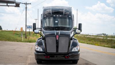 Kenworth T680 sleeper cab front view with dual chrome grille and large windshield, black paint, daytime.