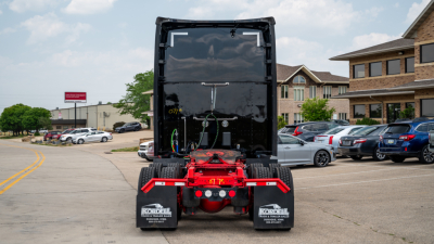 Rear view of a 2019 Kenworth T680 tractor showing dual rear tires, red fifth wheel support, and black sleeper cab with license plate area; vehicle is in a dealership lot.